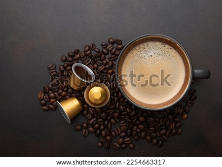 Large cup of coffee with raw beans and ground coffee capsules on brown background.Top view.