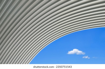Large curve corrugated steel dome roof against 2 mini clouds on blue sky background in minimal style, low angle view with copy space - Powered by Shutterstock