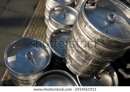 Large damaged 50-liter metal beer barrels are stacked on the terrace of a café. Focus on the barrel on the right