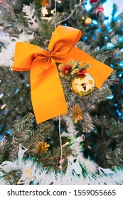 Large Decorative Orange Ribbon Hanging On A Real Christmas Tree Together With Tinsel And And Gold Shiny Balls. Christmas Decorations In The Emporium X The EmQuartier Shopping Mall In Bangkok.