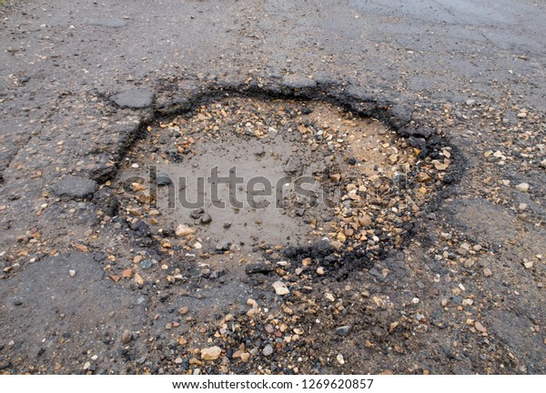 Large deep pot hole in the road. Wisbech Norfolk\
UK. wet poor maintenance. Dangerous to traffic. Damage to\
vehicles