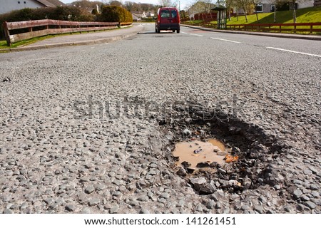 Large deep pothole an example of poor road maintenance due to reducing local council repair budgets