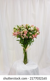 Large Delicate Bouquet Of White And Pink Alstroemerias In Transparent Glass Vase. Festive Bouquet Stands In Vase On Stand Wrapped In White Cloth. Floral Concept. No People.