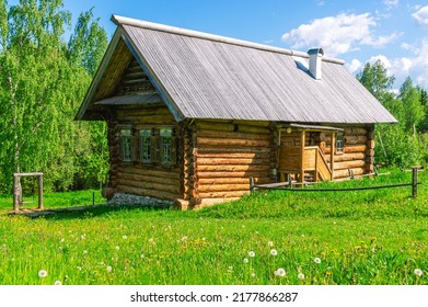 Large diameter logs and windows in a rustic log house built in the 19th century. Dark log walls of the house. Rustic architecture. A house in the village on a background of green grass and blue sky.
