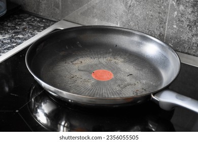 Large dirty Teflon pan in black and silver color for cooking and frying. On the black induction stove in the kitchen