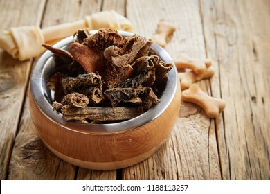 Large Dog Bowl Of Dirty Tripe, Stomach Or Rumen On A Rustic Wooden Floor With Doggy Biscuits And A Puppy Chew In A High Angle View Conceptual Of Animal Nutrition