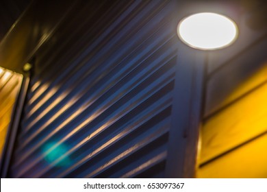 A Large Door To The Garage From The Blinds Is Illuminated By A Lantern, A Night Photo, A Flare Of Lamps