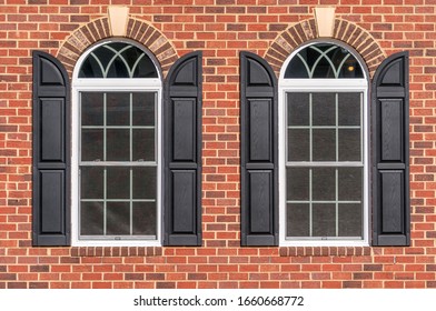 Large double pane hung arched sash windows with white frame, muntins separating the panels, brick sill and lintel, decorative crown stone, arched black shutters on a brick facade luxury American home