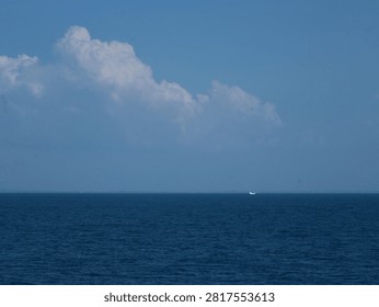 Large dramatic cloud formation over a calm blue ocean with a small fishing boat on the horizon. Peaceful seascape featuring natural light, open water, and vast blue sky