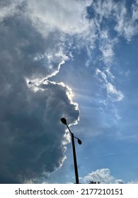 Large Dramatic Dark Clouds Impending Storm Covering Sun With Blue Sky Behind And Tall Black Shadowed Lamp Post