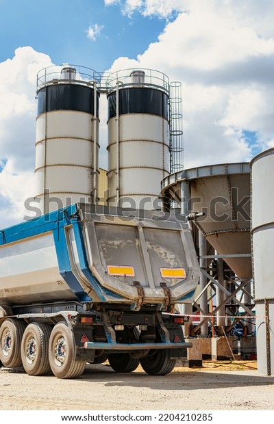 Large dump truck near the concrete\
factory. Car tonar for transportation of heavy bulk cargo.\
Provision of crushed stone and gravel for concrete\
production