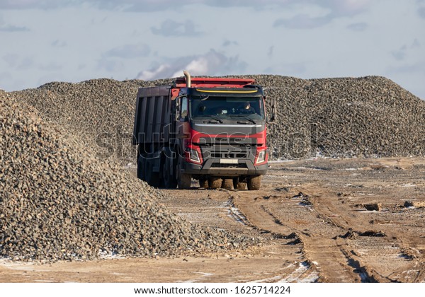 A large dump truck rides on the territory of the\
future construction of the highway against the background of large\
piles of rubble