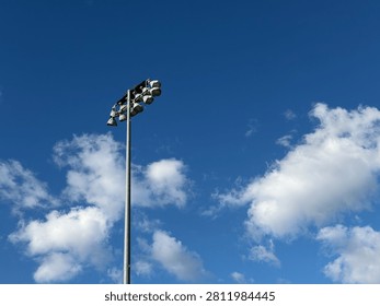 A large eagle nest sits on top of a tall sports field light pole against a clear blue summer sky.