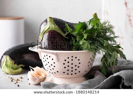 large eggplants with garlic, parsley and dill in a white colander, close up