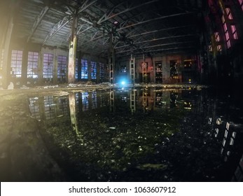 Large Empty Abandoned Warehouse Building Or Factory Workshop At Night With Reflection In Water And Light Effects, Abstract Ruins Background