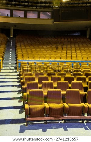 Large Empty Auditorium Inside Abandoned City Hall With Rows Of Worn Vintage Theatre Seats, Blue Carpet Aisles, Upper Balcony Level, And Faded Upholstery In A Neglected Historic Venue Space