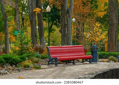 A large empty bench in a city park or garden. Red wooden bench and metal urn