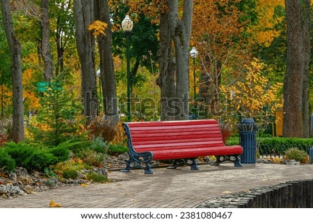 A large empty bench in a city park or garden. Red wooden bench and metal urn