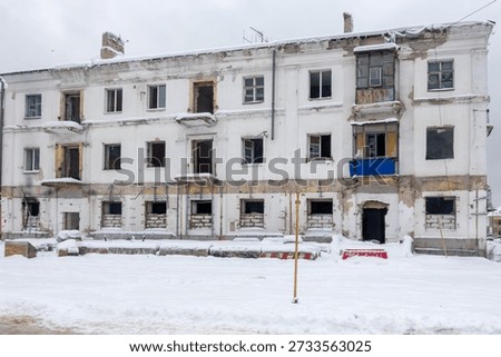 A large, empty building with a blue tarp on the roof. The building is covered in snow and has many windows