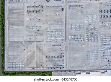 Large Empty Car Factory Car Park, Aerial View Top Down. Large Concrete Car Park With Many White Cars Taken On Sunny Afternoon.