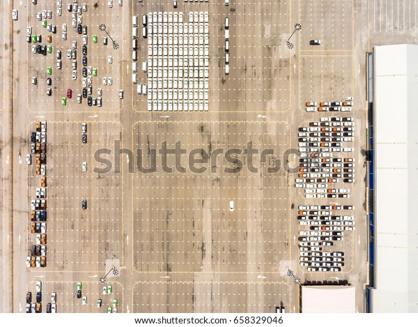 Large empty car factory car park, aerial view\
top down. Large concrete car park with many white cars taken on\
sunny afternoon.