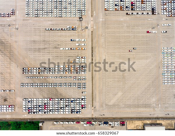 Large empty car factory car park, aerial view\
top down. Large concrete car park with many white cars taken on\
sunny afternoon.