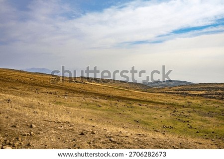 A large, empty field with a few rocks scattered around. The sky is cloudy and the sun is not visible
