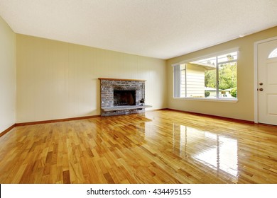 Large empty living room  interior with brick fireplace, polished hardwood floor and white entrance door.