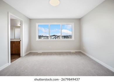 Large, empty room with a window overlooking a city. The room is clean and uncluttered, with a white wall and a light-colored carpet. The window lets in natural light
