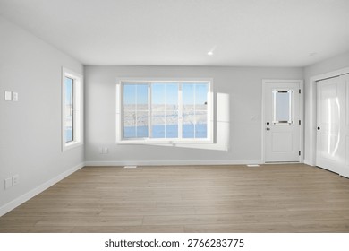 Large, empty room with a window overlooking a body of water. The room is clean and well-lit, with a wooden floor and white walls. The open door and window let in natural light, creating a bright