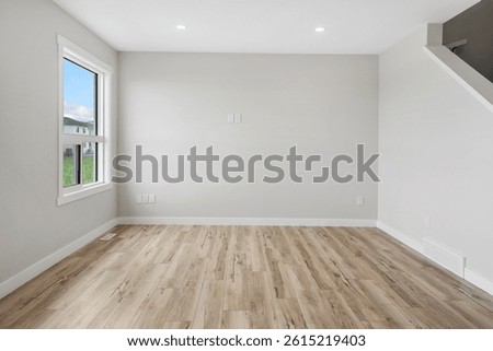 Large, empty room with a window and a staircase. The room is very clean and has a very simple design