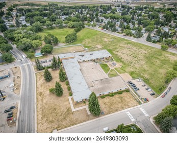 Large empty lot with a school building in the middle. The lot is surrounded by a fence and has a parking lot with several cars
