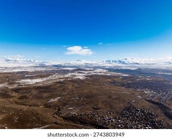 A large, empty, snow-covered plain with a few houses in the distance. The sky is clear and blue