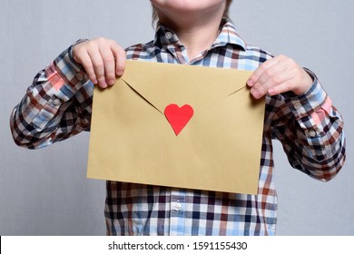 Large envelope with a red heart in children's hands. Close-up