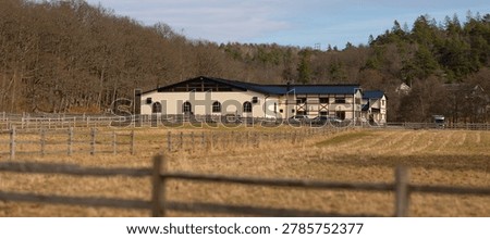 Large equestrian stable building beyond fenced fields in rural countryside
