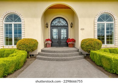 Large estate home on lush green grass landscaping blue sky elegant house has yellow paint three car garage rounded shape heavy wooden front door arched doorway and brick trim - Shutterstock ID 2298666755