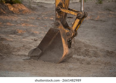 A large excavator is engaged in digging at a construction site in the late afternoon. The sandy soil is disturbed as the machine operates efficiently