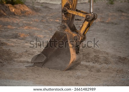 A large excavator is engaged in digging at a construction site in the late afternoon. The sandy soil is disturbed as the machine operates efficiently