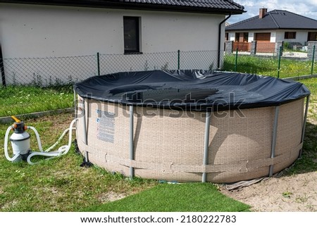 Large expansion pool with a diameter of 3.96 meters with black cover, set in the backyard next to the house.