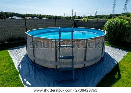 A large expansion pool with a diameter of 3.96 meters, placed on a sheet of plastic on the grass in the garden.