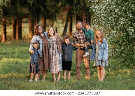Large family of father, mother, two brothers and three sisters standing and sitting on a green field in summer, full length portrait.