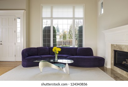 Large Family Living Room With Suede Sofa, Glass Table In Front Of Large Double Pane Window With Daylight Coming In To Room