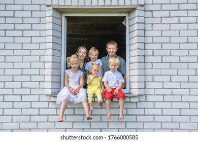 A Large Large Family Poses From The Window Of Their Home.