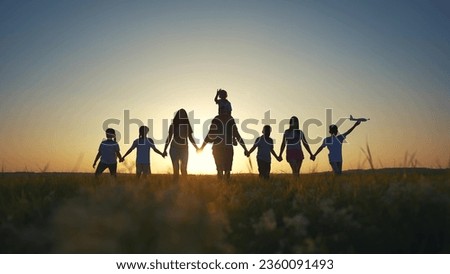 large family walks across field holding hands. happy family childhood dream concept. lifestyle family walks across the field on the grass at sunset and hold each other's hands dark silhouettes