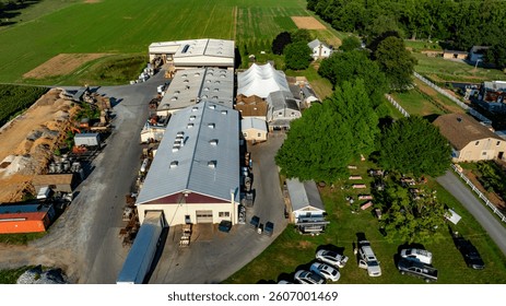 Large farm complex with multiple storage buildings and equipment surrounded by lush green fields is illuminated by the sun. This vibrant rural setting emphasizes agricultural productivity