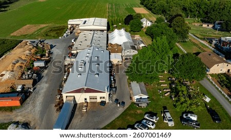 Large farm complex with multiple storage buildings and equipment surrounded by lush green fields is illuminated by the sun. This vibrant rural setting emphasizes agricultural productivity