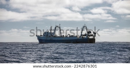 Large fishing trawler conducts industrial fishing in the open ocean. Old fishing vessel on the horizon is operating in southern oceanic waters. 