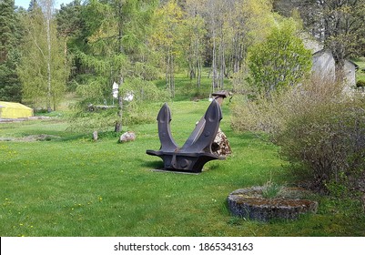 Large five tons ship anchor is mounted on green grass on a sunny spring day