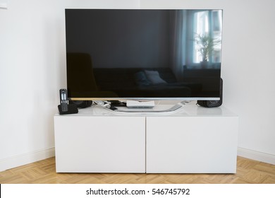 Large Flat Screen Television On White Cabinets Standing In The Corner Of A Living Room Against The Walls, Blank Screen With Copy Space And Reflection