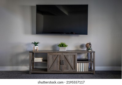 Large Flatscreen Television On Grey Wall With TV Stand Decorated With Books And Assorted Items